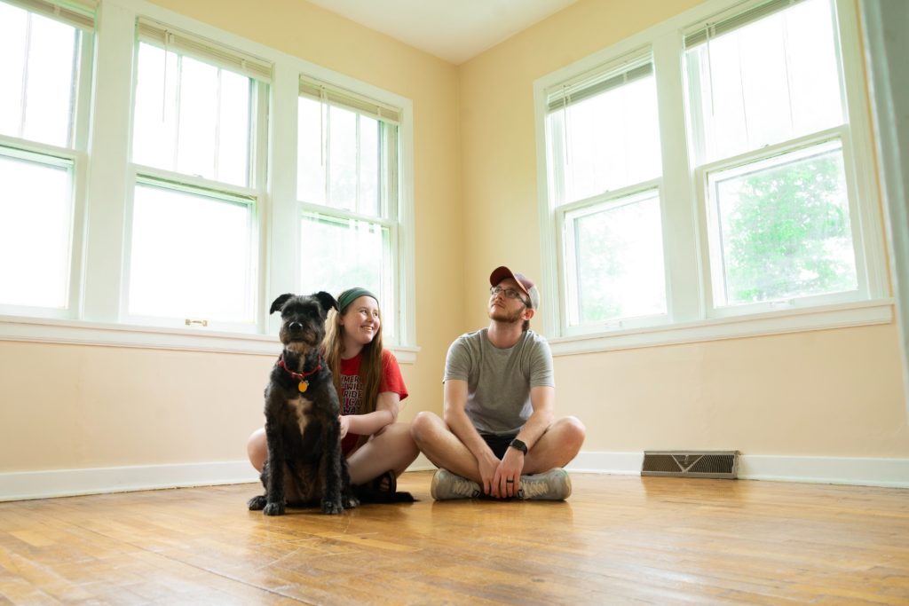 couple with dog sitting on the wooden floor in an empty room smiling with their dog