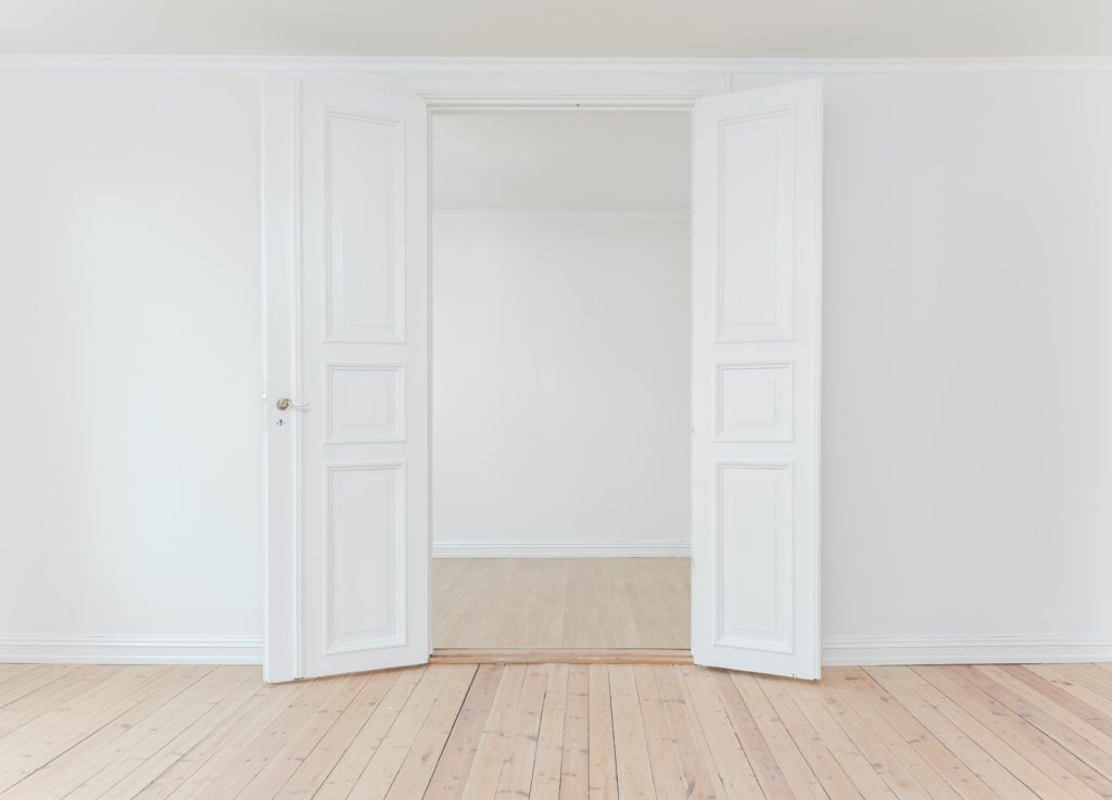 white wall with white double pannel doors open wide into the next room which also has white walls and light wooden flooring