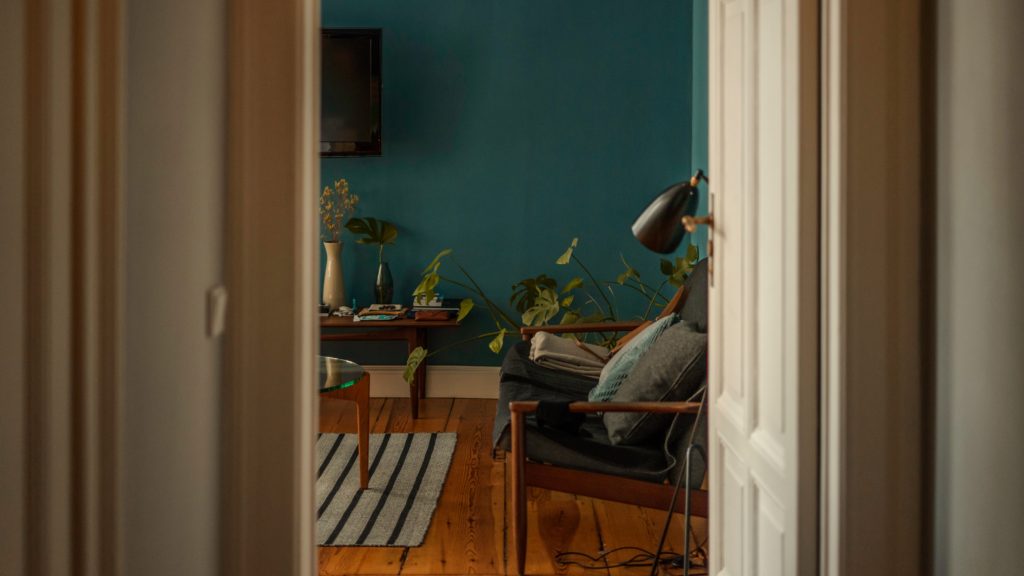 image looking thorugh door into room with teal painted walls and a dark wooden floor. You can see half a wooden chain with blue upholstery