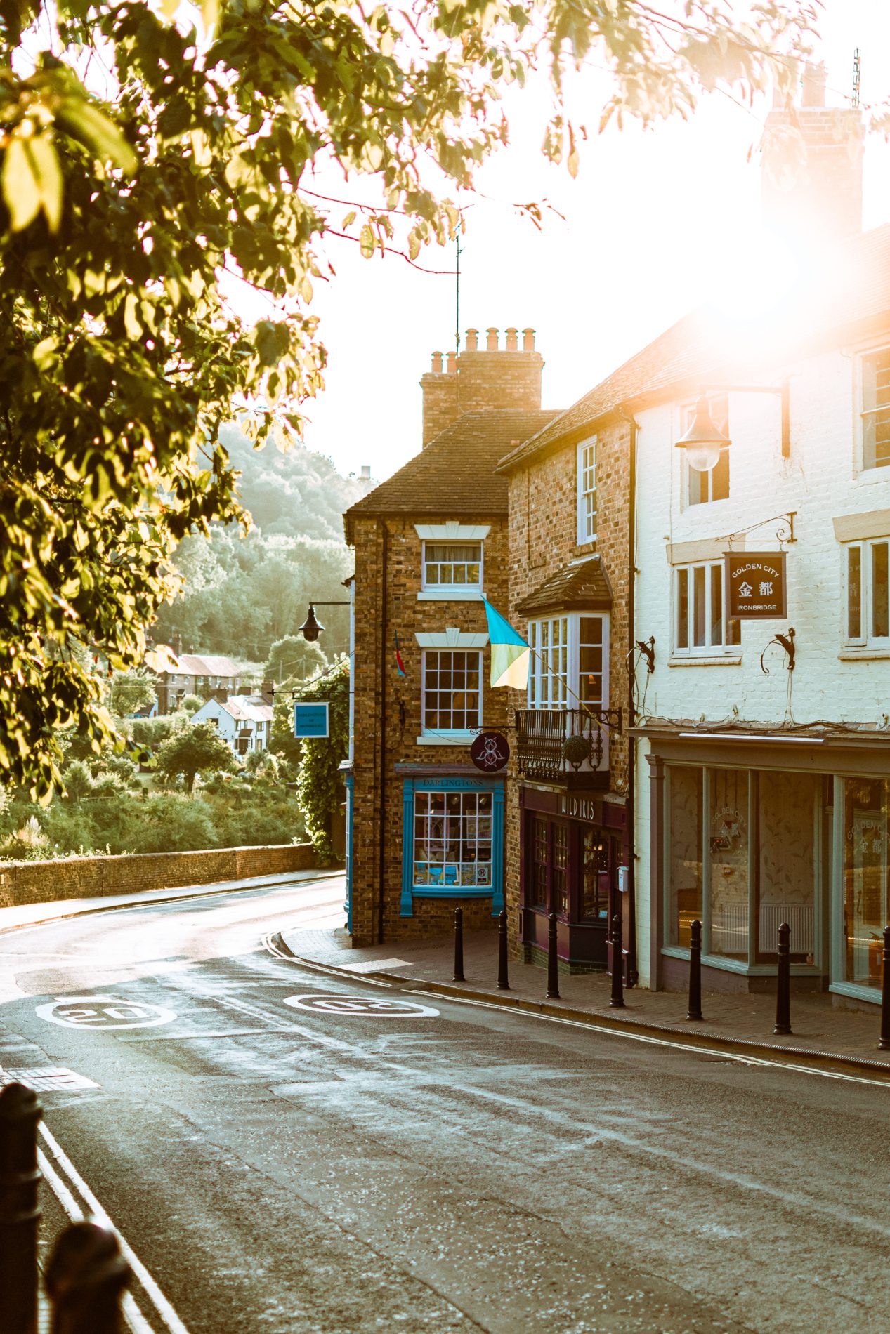 Ironbridge highstreet with trees bu the river in the background and low sun shining brightly just behind the stone buildings