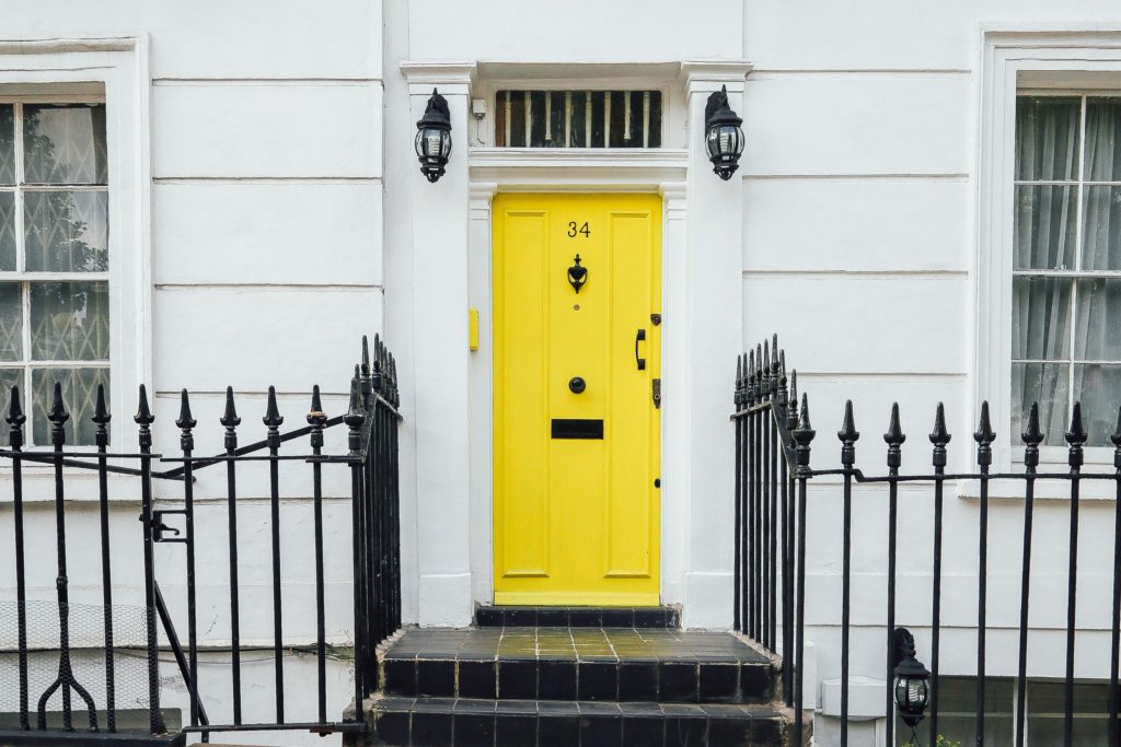 Image of a a bright yelloe front door on a white house with black steps leading up to the door.